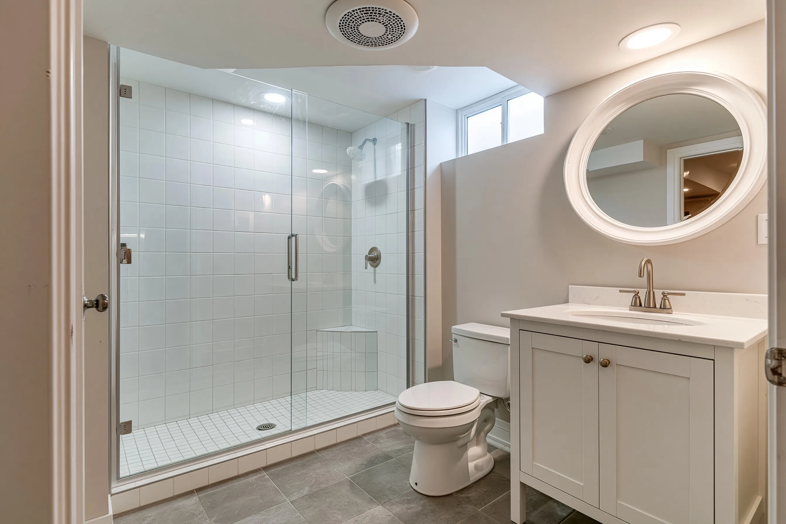Finished basement bathroom with a walk-in tiled shower, a white vanity, a light grey tile floor and an exhaust fan grille