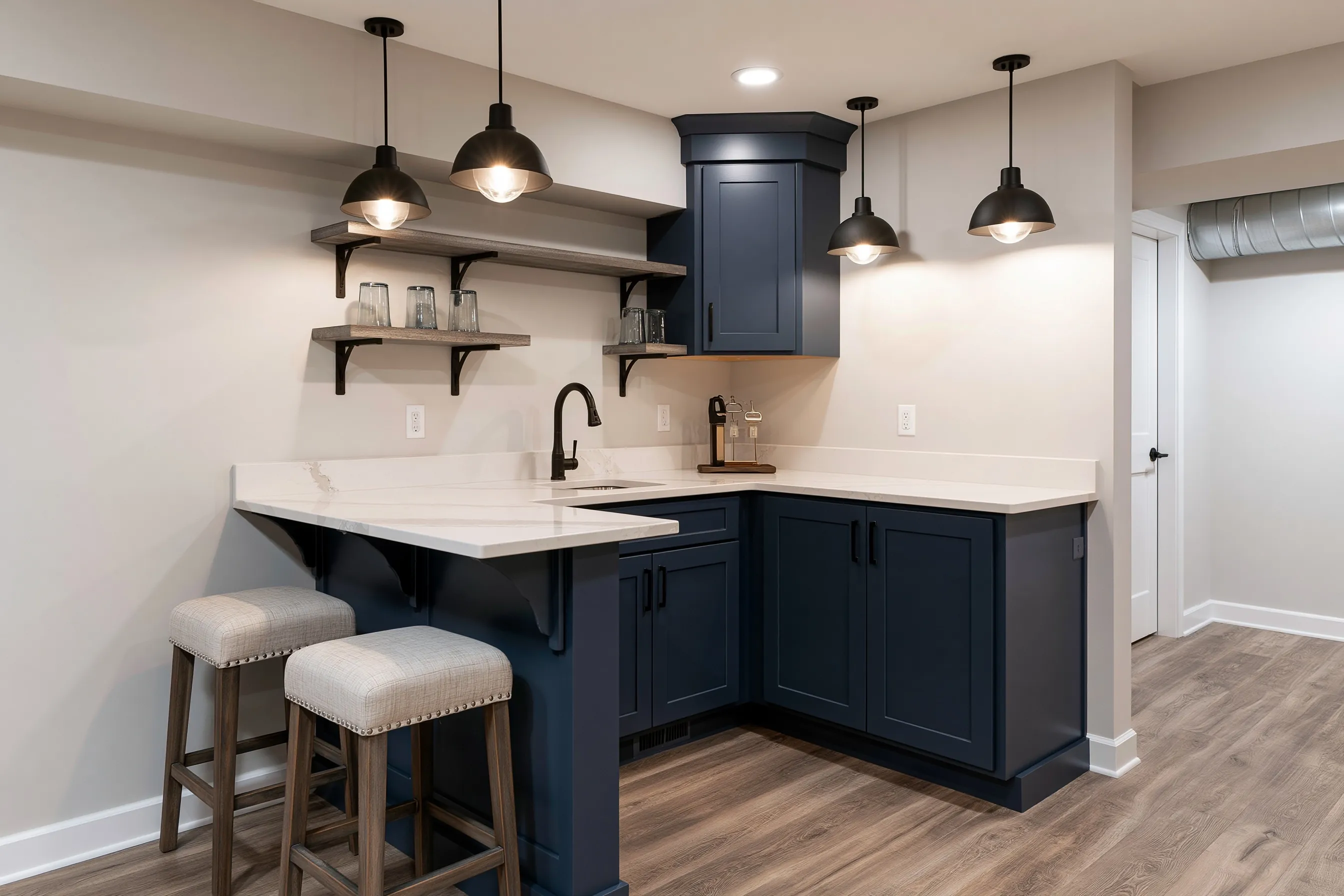 Small L-shaped basement wet bar with a sink, shaker cabinets, floating shelves, two counter stools and pendant lights